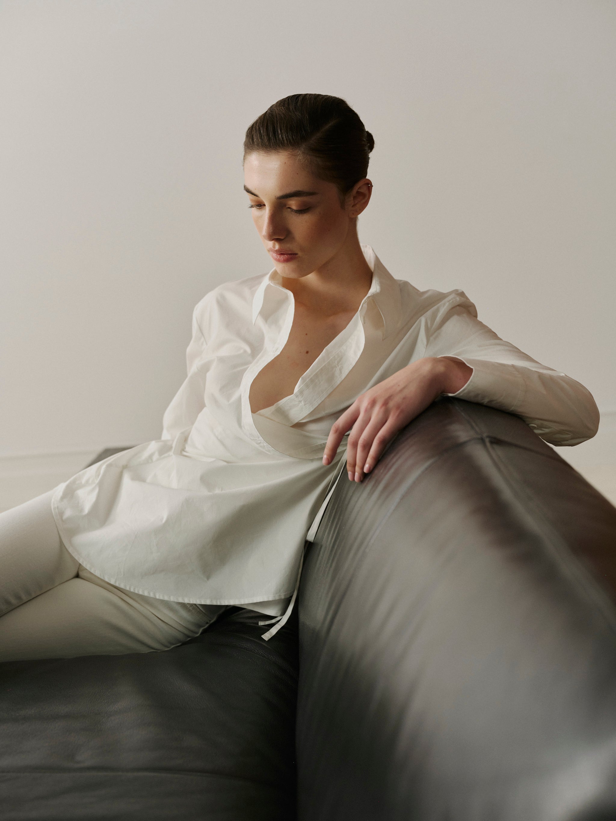 Woman in a white shirt sitting on a gray couch against a plain wall.