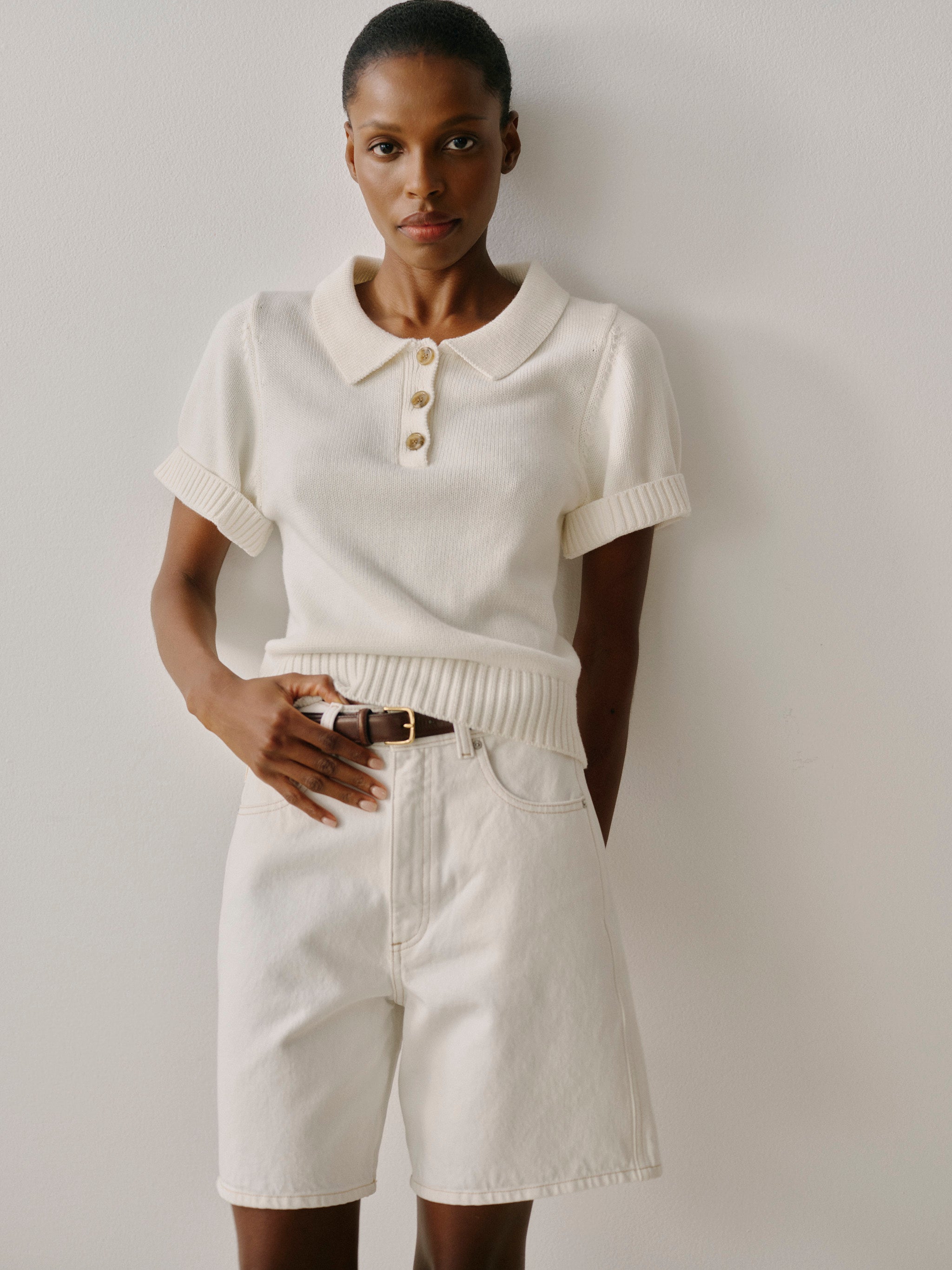 Person wearing a white knit polo shirt and light-colored shorts against a plain background