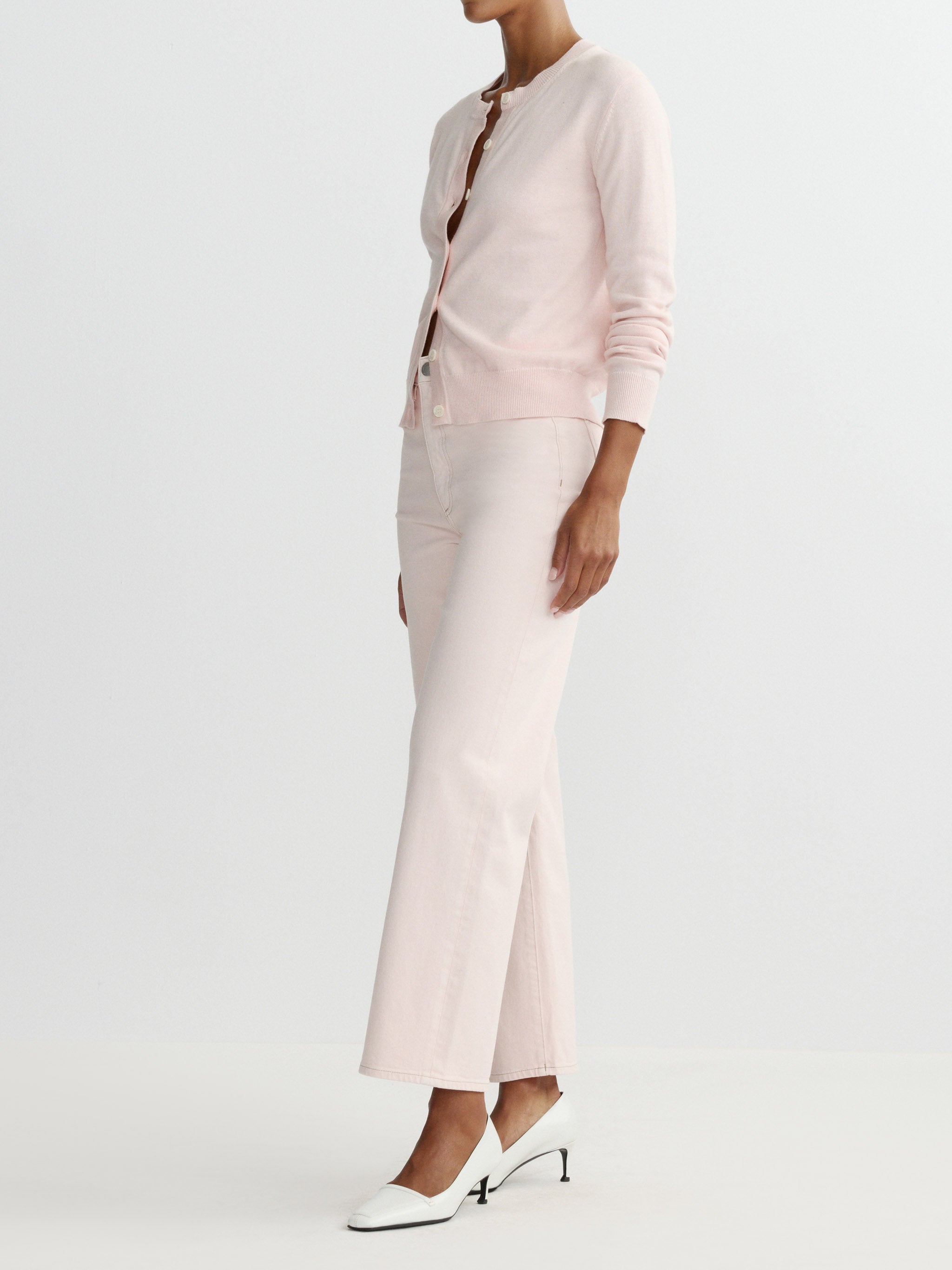 Person wearing a light pink outfit with a matching cardigan and pants on a plain background