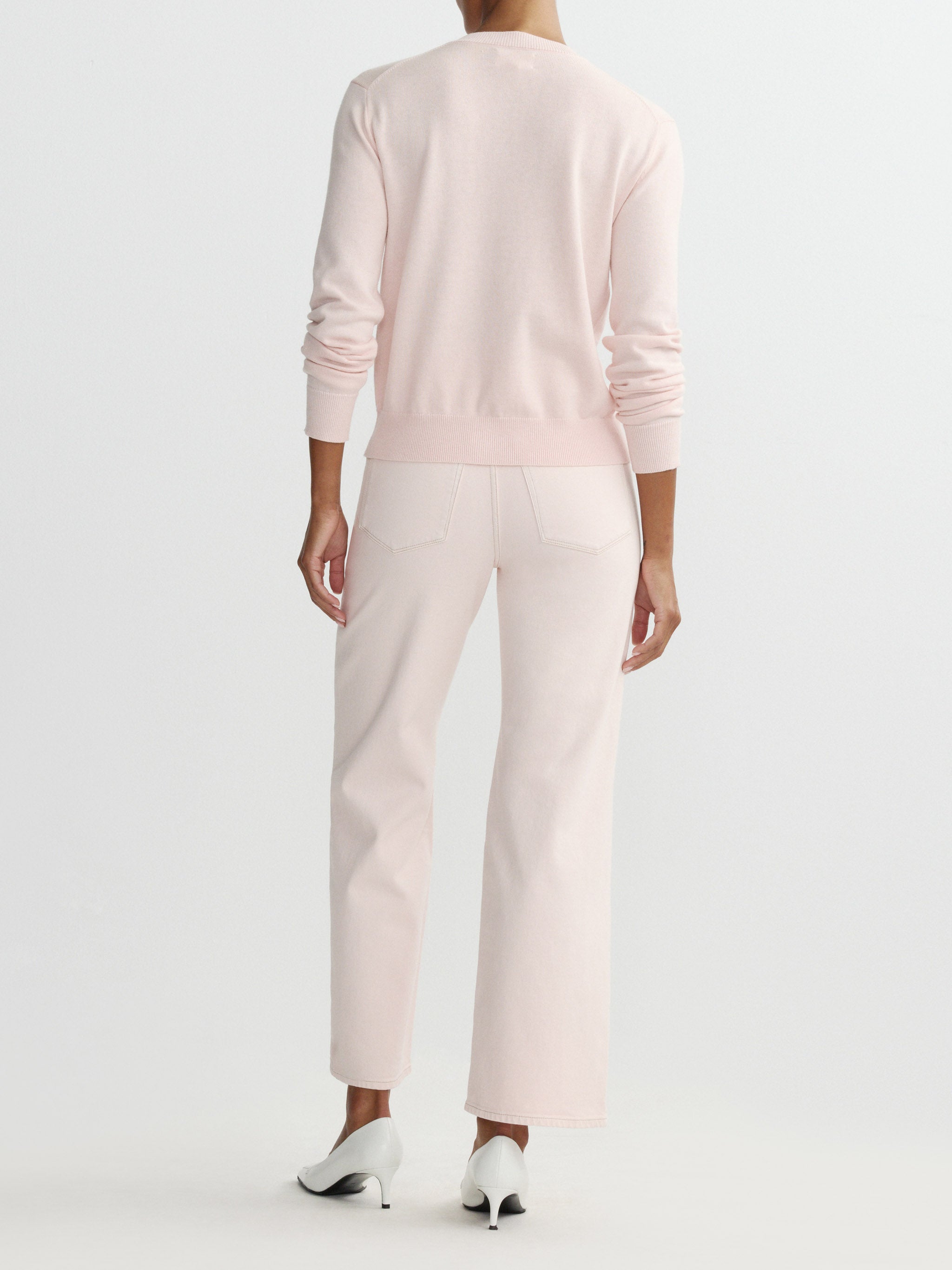Person wearing a light pink sweater and pants on a white background