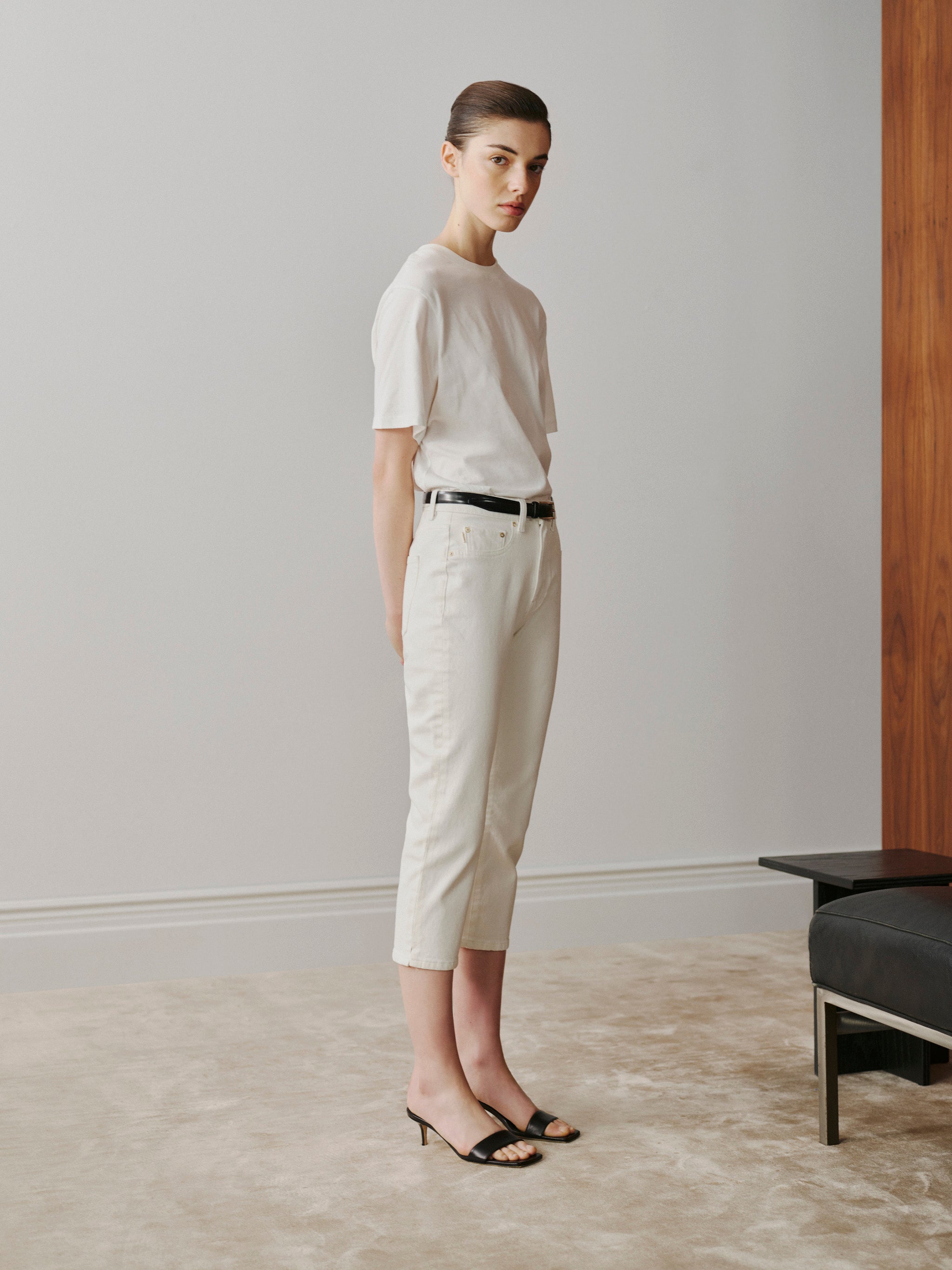 Woman wearing a white t-shirt and beige pants standing in a minimalistic room.