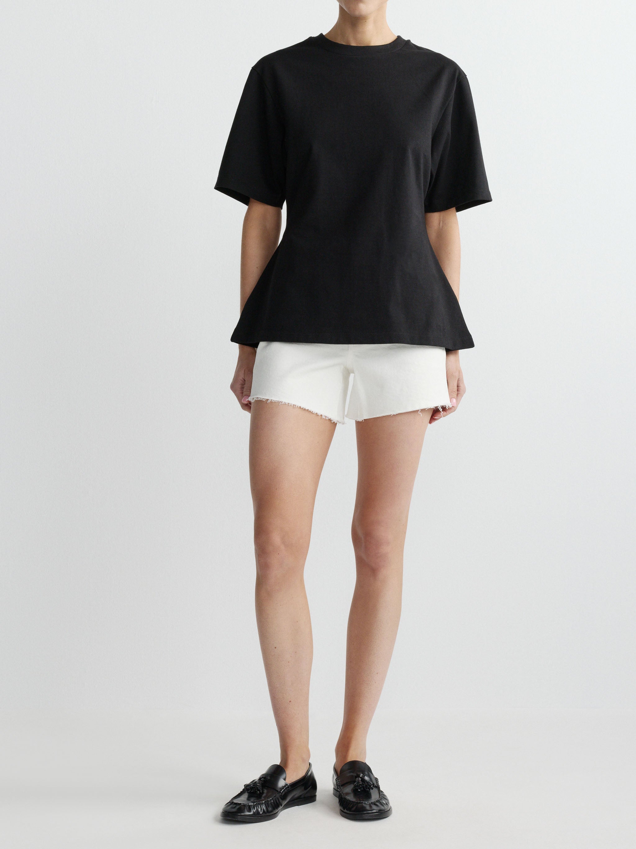 Person wearing a black t-shirt and white shorts on a plain background