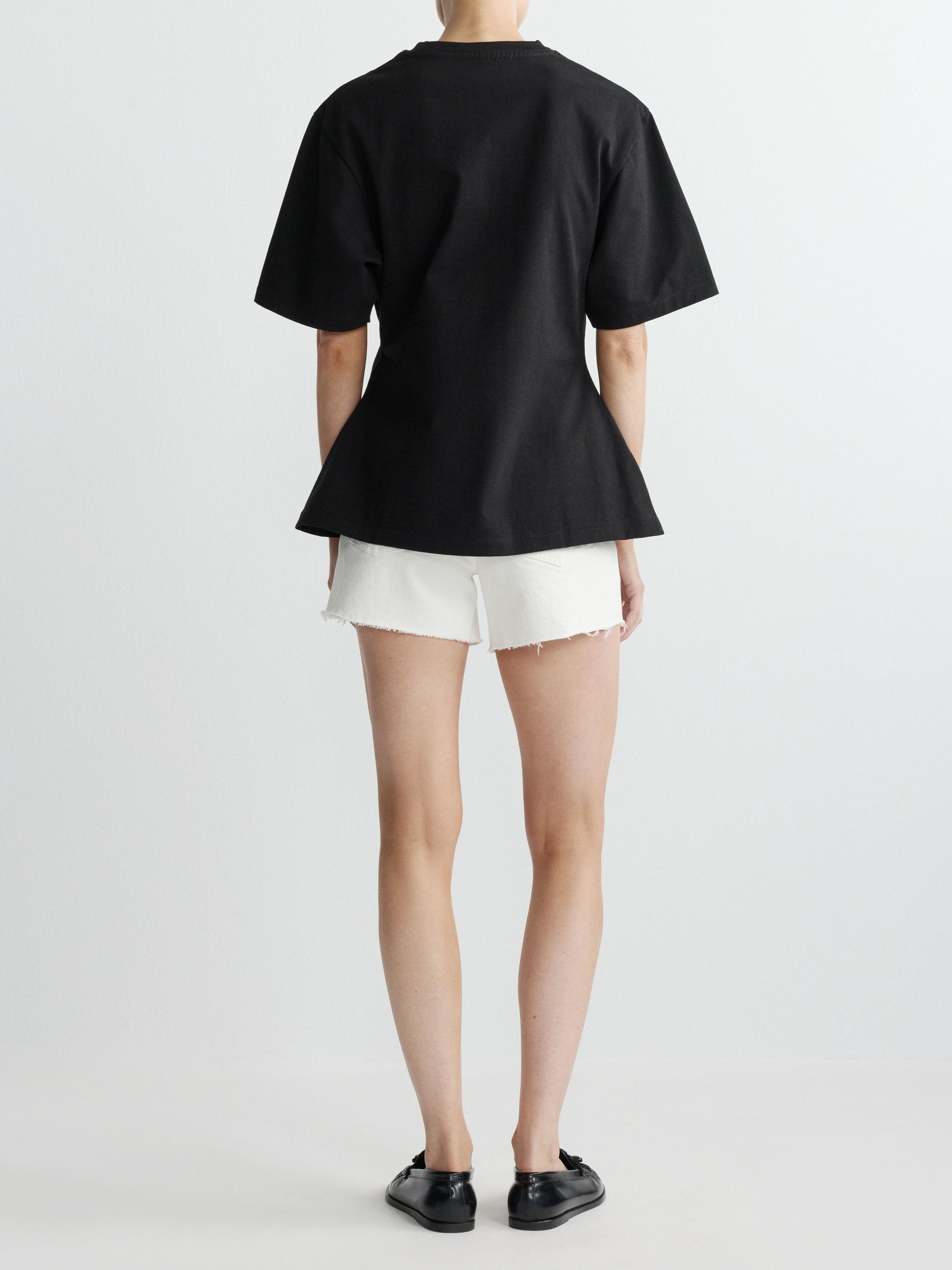 Person wearing a black t-shirt and white shorts on a plain background