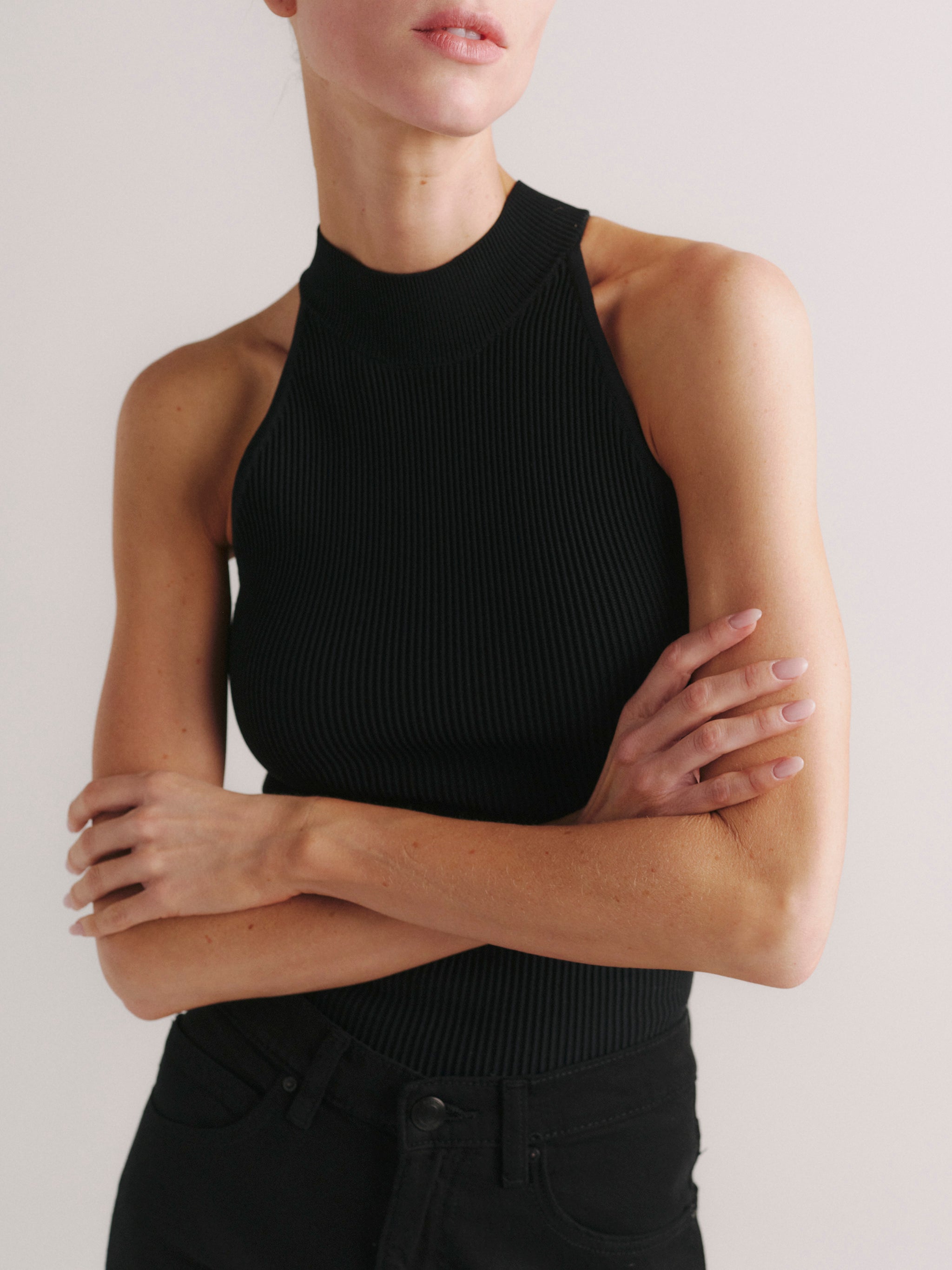 Mock Neck Top Instasculpt Rib in Black on a model, arms crossed, studio portrait close-up.