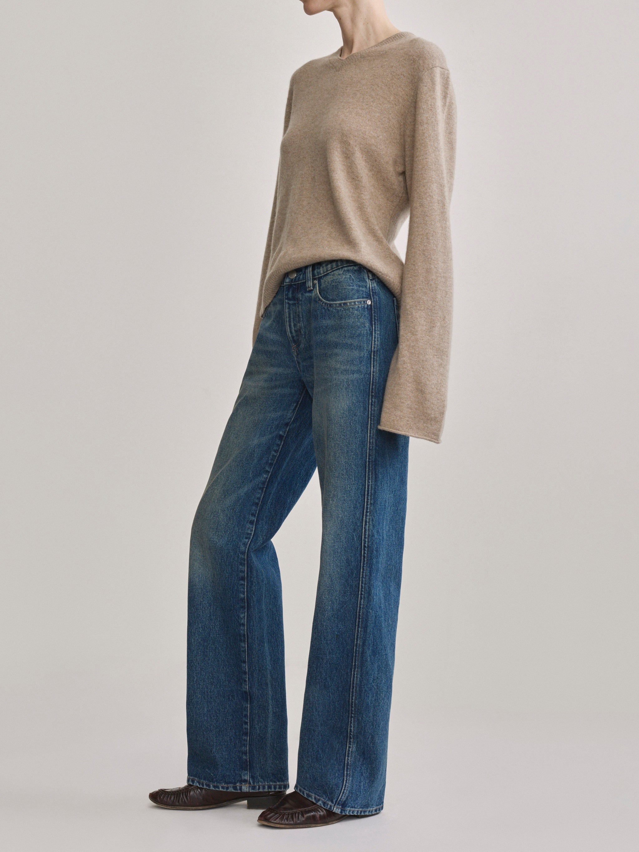 A model wearing a beige knit sweater and blue wide-leg jeans, standing against a light gray studio background.