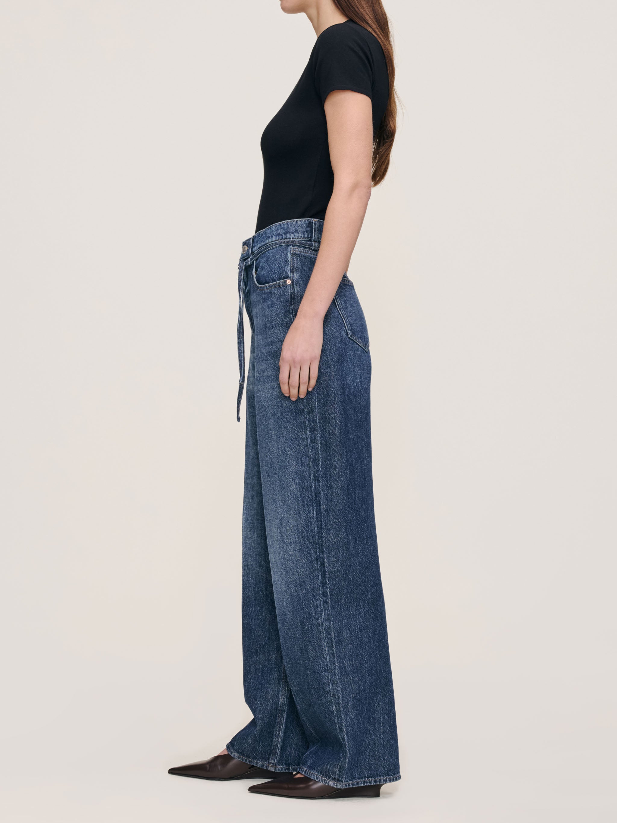 Person wearing blue jeans and a black top on a plain background