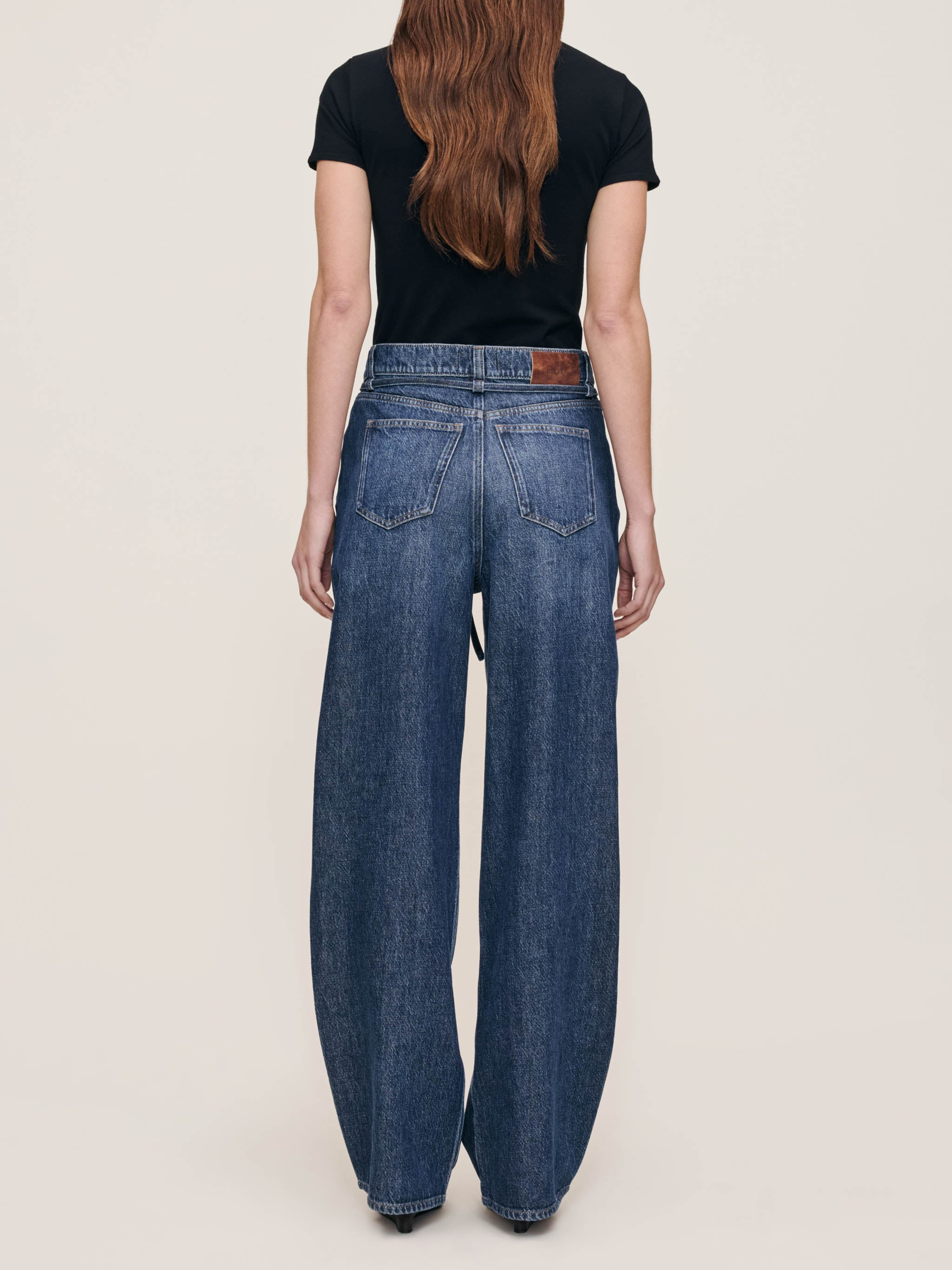 Person wearing blue jeans and a black top on a plain background