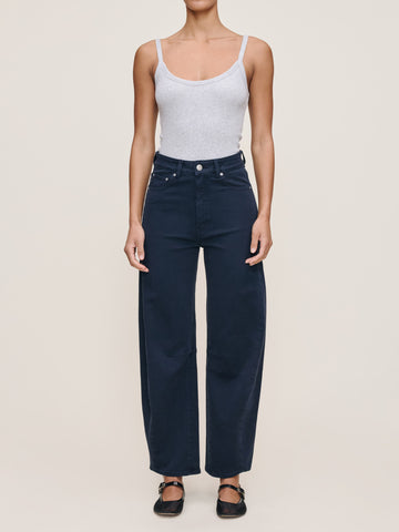 Person wearing a white tank top and dark blue jeans on a beige background