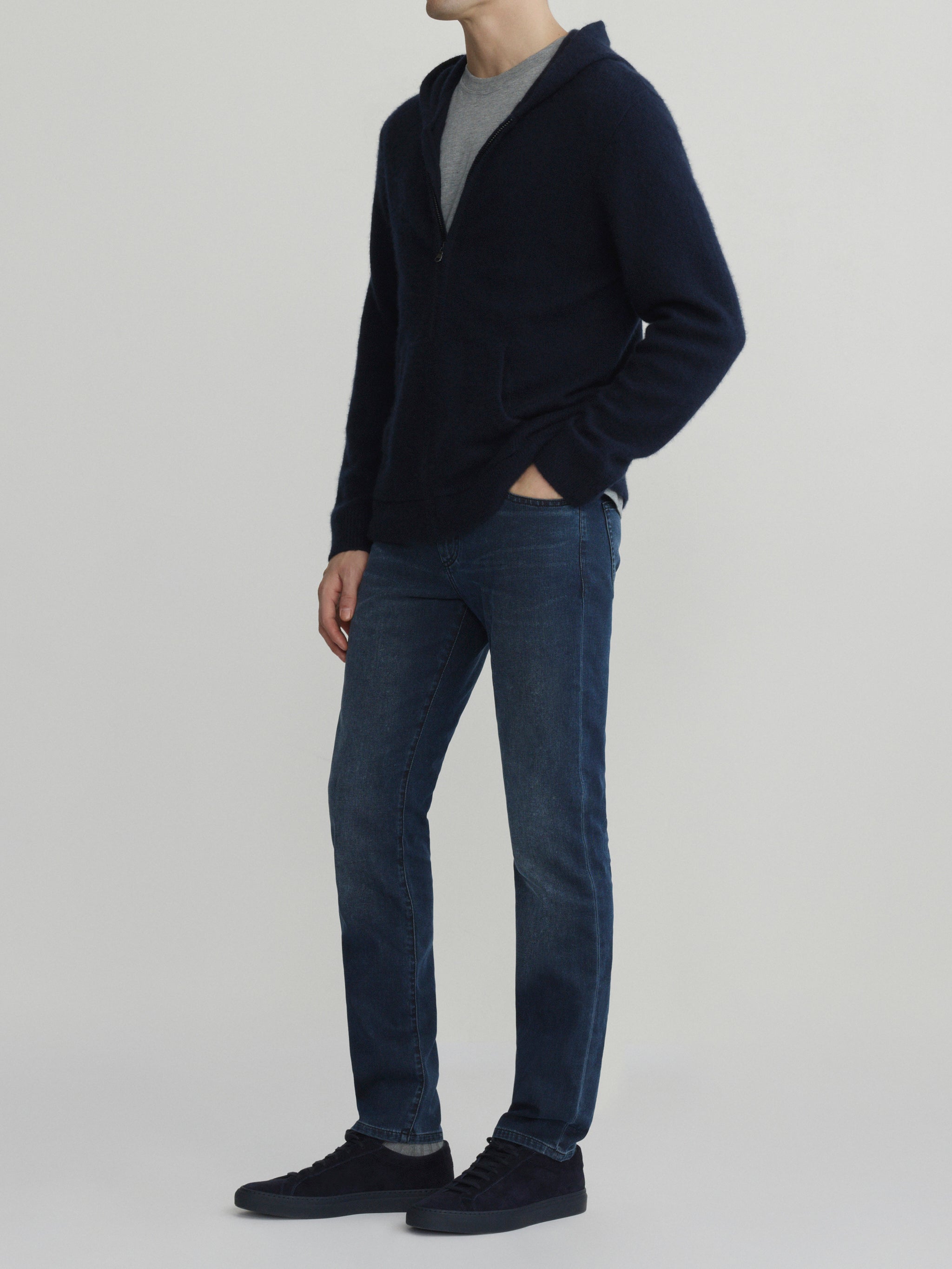 DL1961 men's Nick Slim jeans in faded blue-grey 'Cold Forge', three-quarter front view with navy zip cardigan, hand in pocket.